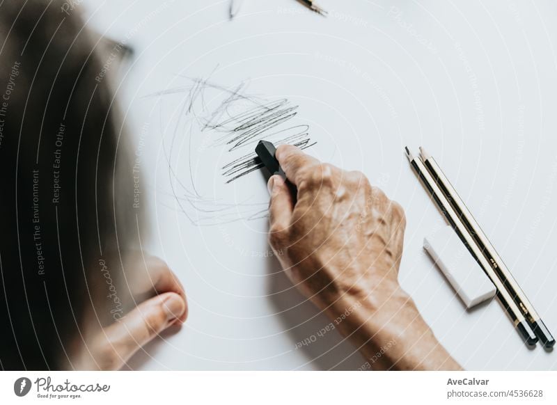 High angle view of a senior Caucasian woman drawing sketches in studio. Creativity, education and people concept,cognitive functions clock drawing self assessment test at home with positive results