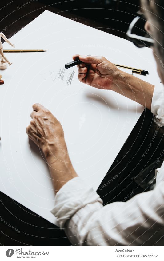 High angle view of a senior Caucasian woman drawing sketches in studio. Creativity, education and people concept,cognitive functions clock drawing self assessment test at home with positive results