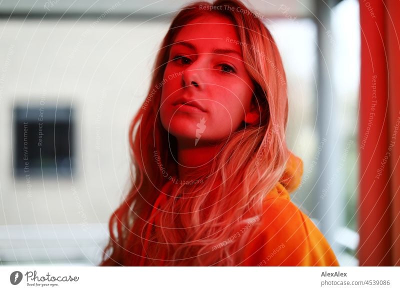 Portrait of a young, slim woman with long blond hair in the living room in front of the window, she is illuminated with red light Woman Young woman Large Blonde