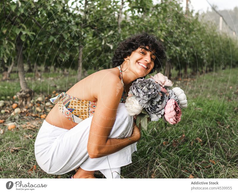 Happy female with bunch of flowers hugging knees in garden woman bouquet peony lush bloom happy charming gentle blossom embracing knee content plant fruit