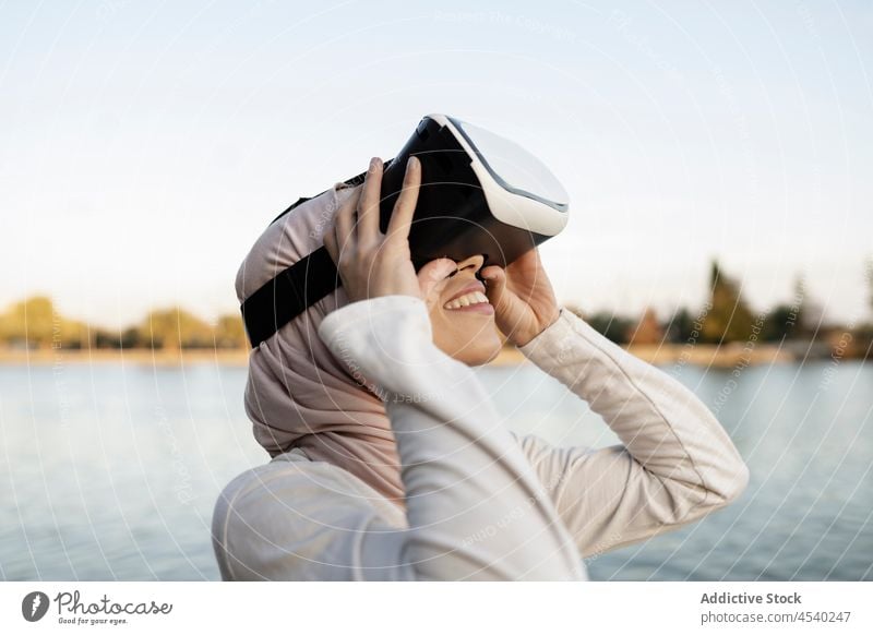 Arab woman in VR headset on embankment vr goggles virtual reality river simulate cyberspace water female arab muslim waterfront modern contemporary headscarf