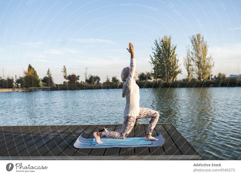 Graceful Arab woman doing Anjaneyasana pose on pier meditate anjaneyasana practice yoga posture balance serene female harmony hijab crescent lunge on knee zen