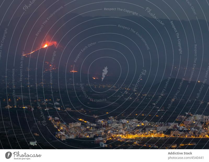 Small settlement in mountainous valley with erupting volcano house range night landscape lava highland town scenery travel residential village picturesque