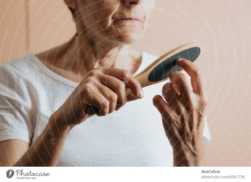 old woman filing her nails, removable flesh colored background.Elderly woman is getting a manicure.Woman prepare nails for gel polish filing gel down with filer.A woman makes her own manicure.