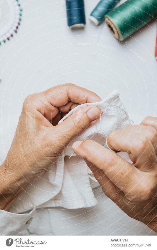 Seamstress old hands sewing and doing works. Cloth working and sewing. Lightful image, copy space, threads of different colors background. senior textile