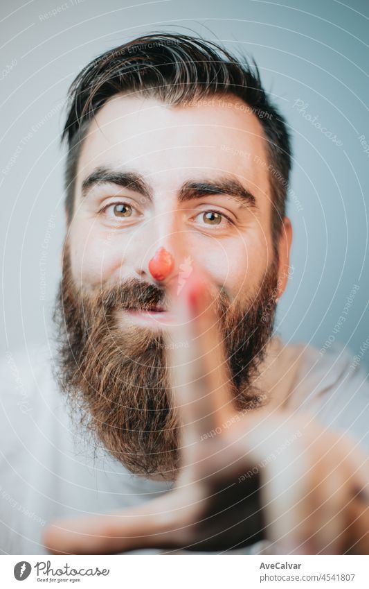 Young hipster man with beard and red paint in the nose smiling and playing portrait, young artist concept, close up portrait, funny image, creativity and fun