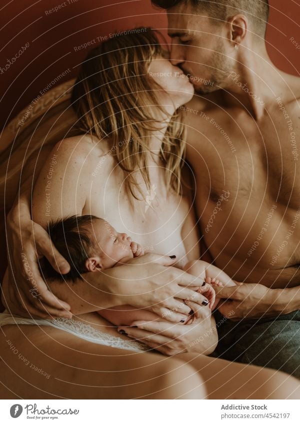 Happy naked couple with baby cuddling on bed family cuddle newborn kiss breastfeed love together embrace relationship happy close wife husband adult nude care