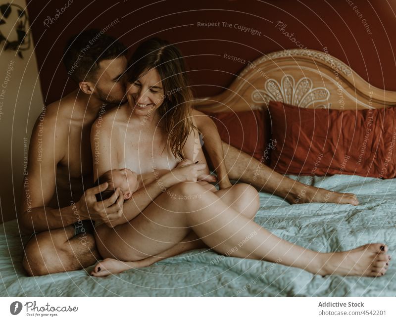 Happy naked couple with baby cuddling on bed family cuddle newborn kiss breastfeed love together embrace relationship happy close wife husband adult nude care