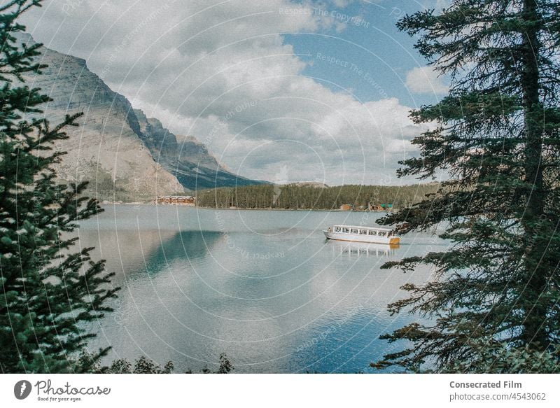 Looking through the woods to a boat on a lake in the mountains with still reflection Reflection in the water Water mountain boat boats travel adventure Lake