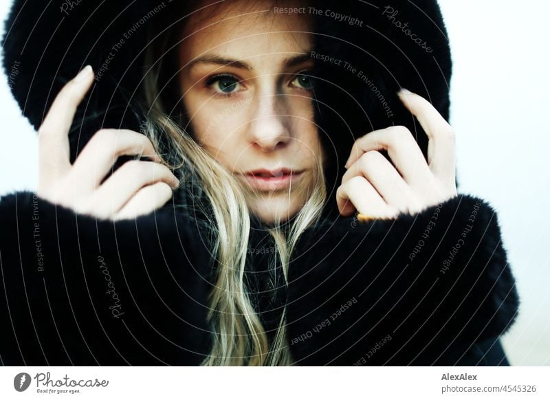 Portrait of a young woman with blond hair standing on a foggy beach in a fur coat with hood Woman Young woman Large Blonde Long-haired pretty daintily Slim