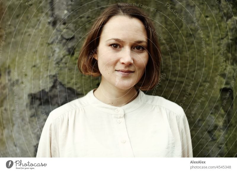 Portrait of a young woman in the park in autumn in front of a natural stone wall Cheerful Ease Beige Green Beautiful weather Moody Face of a woman free time