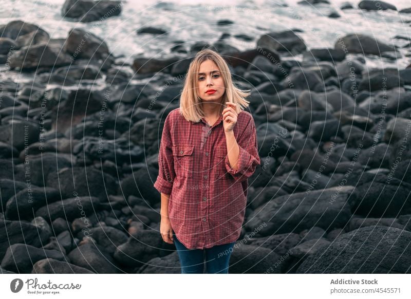 Pensive woman standing on rocky coast with windy weather water sea shore coastal nature adventure pastime trip stone formation leisure environment seaside beach