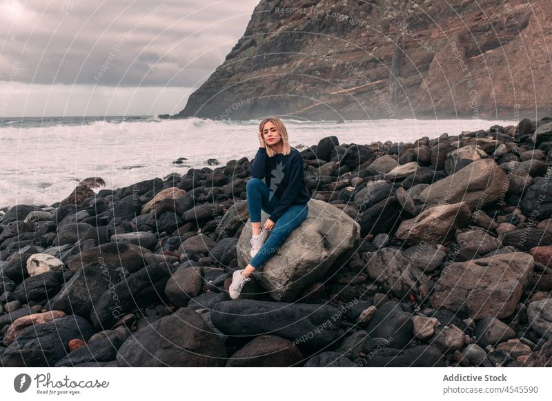 Woman sitting on stony shore woman water sea rocky coast coastal nature adventure pastime trip stone formation leisure environment seaside beach seashore