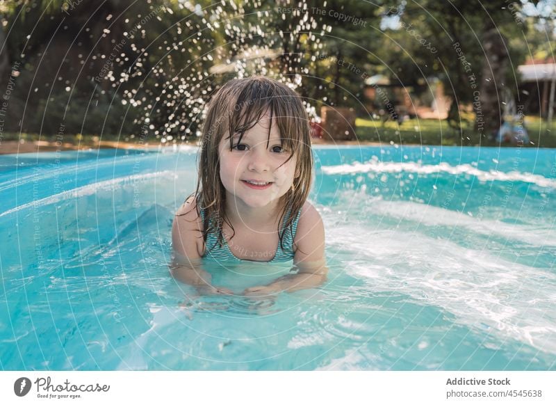 Cute positive kid smiling at camera in swimming pool child smile vacation holiday girl yard happy summer poolside water cute childhood resort wet hair blond