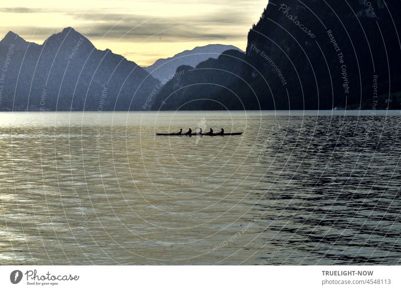 Weather change at Vierwaldstaettersee (Lake Lucerne) Switzerland! Escaping the big rain: 5 unidentifiable rowers in a racing boat in the early morning in front of the imposing backdrop of the Bürgenstock and other mountains.