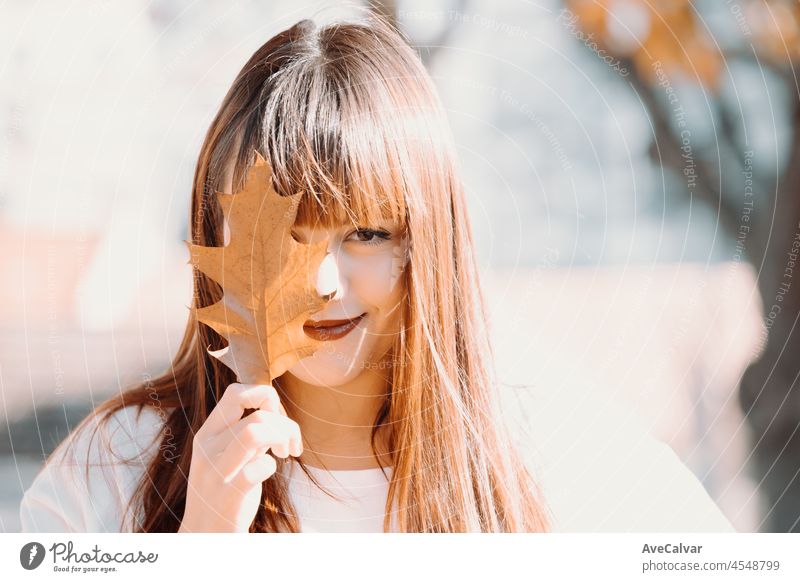 Happy pretty young redhead woman with a cute smile in a white tshirt with a maple leaf in hands. Golden foliage. Autumnal concept, smiling happy, seasonal moment. Close up portrait