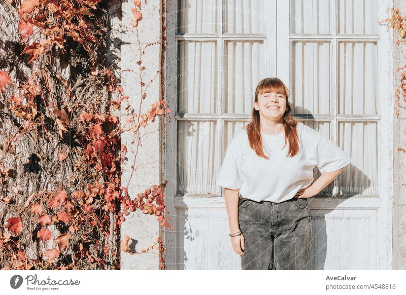 Frontal portrait of a young red head body positive woman, laughing, smiling and having fun in front of a beautiful ancient white house. Happy lifestyle and fun concept. Copy space to add or text.