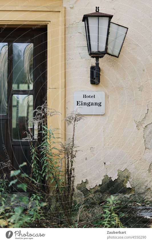 Entrance door of an abandoned hotel, overgrown with plants Hotel Lantern forsake sb./sth. lost places Decline Transience sign Futile Closed broke loss corona