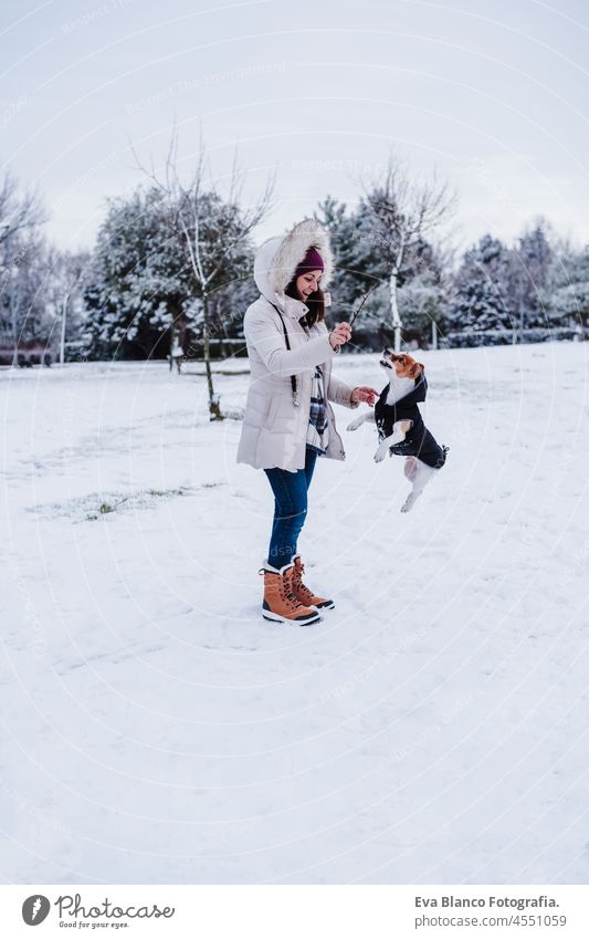 woman in snowy mountain wearing modern coat at sunset. Playing with cute jack russell dog. winter season. Fun in the snow playing jump fun love together