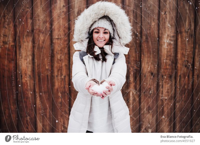 happy woman in city during winter while snowing holding snow ball. woman enjoying outdoors, winter lifestyle. Wood background walking cold playing park