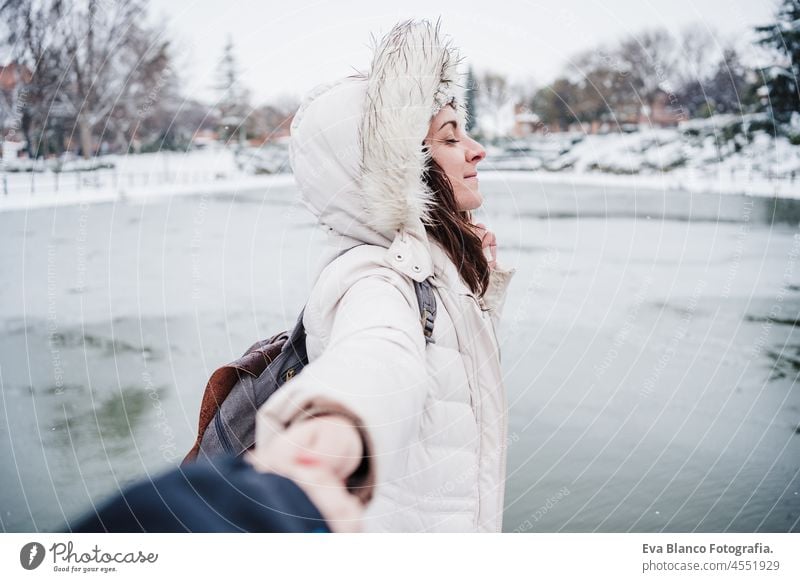 happy caucasian woman holding hand of boyfriend, standing in front of frozen lake during winter season. Love and lifestyle outdoors snow love couple together