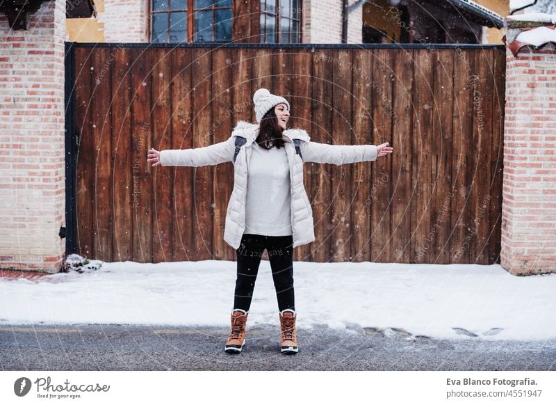 backpacker woman walking in city during winter while snowing. Happy woman with arms outstretched enjoying outdoors cold playing park caucasian mountain