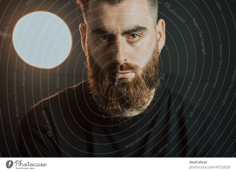 Cinematic shot of a young hipster bearded man with modern hairstyle with cinematic lighting. Attractive man looking serious straight to camera, mental health concept. Depression and anxiety portrait