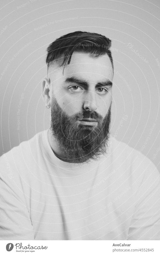 Portrait of a young bearded man smiling to camera with a white background. Cinematic tones and lightning. Sad day, mental health concept, depression and anxiety