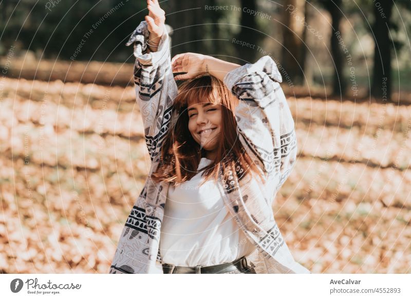 Happy young woman having fun in autumn forest.Woman portrait. Happy girl in white shirt and blue jeans is playing with leaf, looking at camera and smiling. Copy space.Portrait in autumn park.