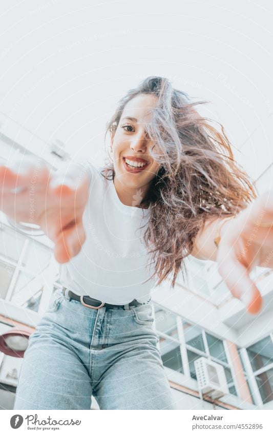 Urban shot of a modeling young african woman with long hair smiling and making poses to camera. City urban concept. Happy day on the city, white shirt blue jeans. Modern outfit styling. Street life.