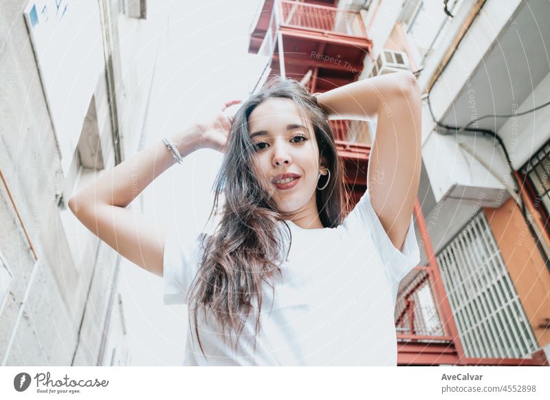 Urban shot of a modeling young african woman with long hair smiling and making poses to camera. City urban concept. Happy day on the city, white shirt blue jeans. Modern outfit styling. Street life.