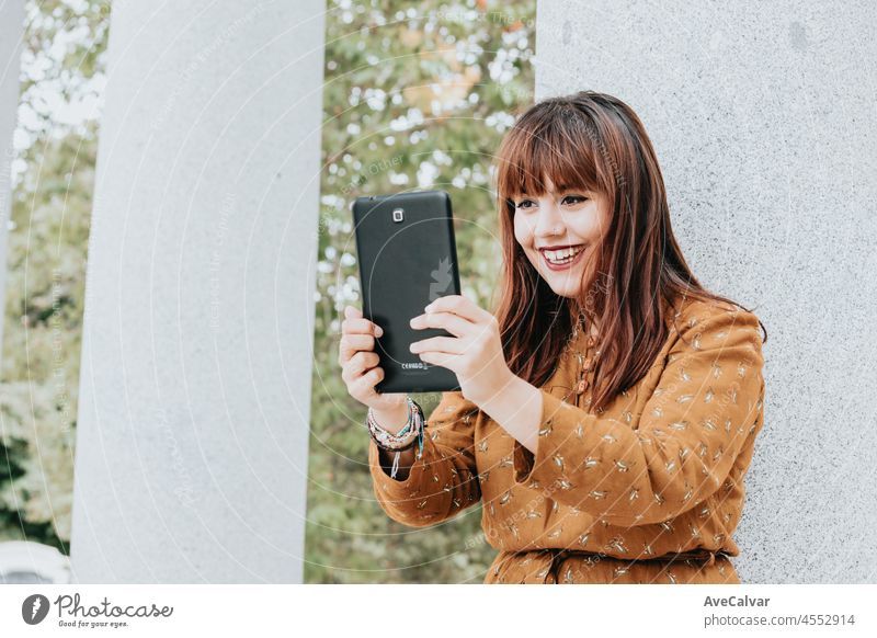 Young hipster red head woman having fun during a video call with the tablet.Day at the park, copy space, rest day. Beauty dress. Internet connection concept. Modern style during a sunny day.