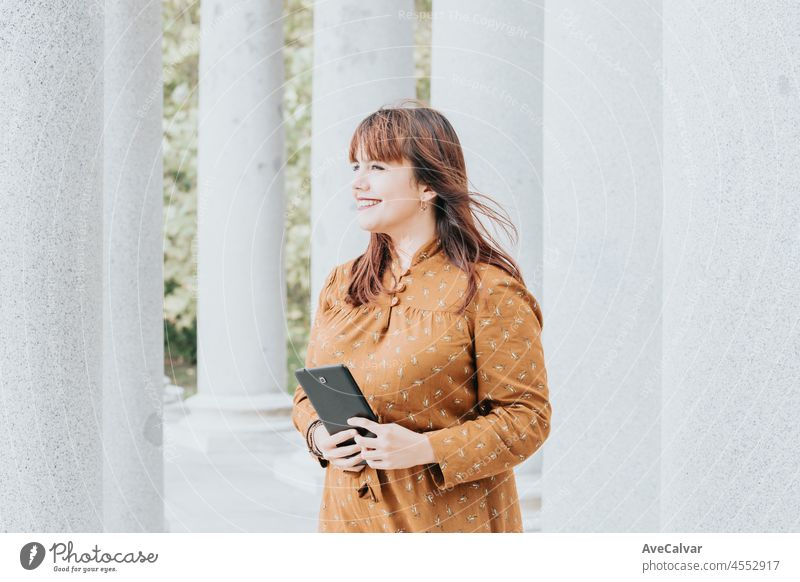 Portrait of a young red head woman looking away from camera while smiling. Windy day. Autumnal dress colorful days. Day at the park, connect wireless video call. Beauty woman long hair