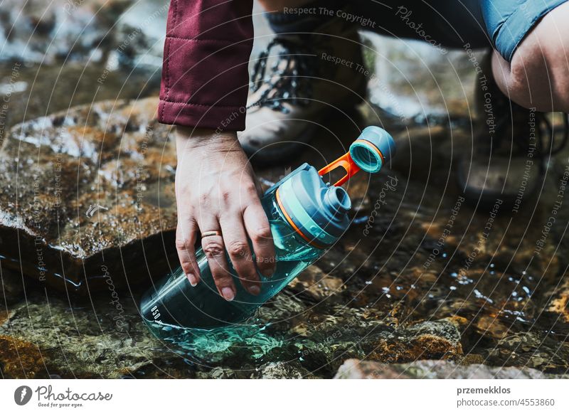 Woman taking pure water to bottle from mountain stream during trekking in mountains adventure trip travel hiking thirsty vacation journey crouching summer