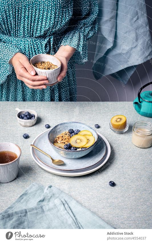 Woman adding granola to bowl with fruit woman blueberry kiwi food breakfast nutrition portion morning female tea homemade muesli ingredient healthy food spoon