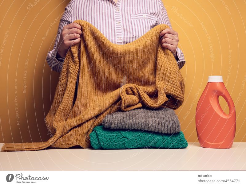 adult woman folds washed dry clothes on a white table, next to a plastic bottle with liquid washing gel, yellow background detergent chemical hygiene clean