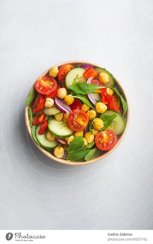 Vegetarian chickpea beans salad prepared with tomatoes and cucumber in a paper bowl. Zero waste dishware, top view lunch cardboard office chick-pea arugula