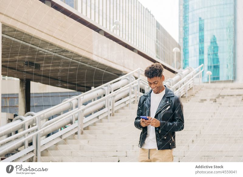 Black smiling man with smartphone on bridge staircase cellphone using texting cheerful smile step ladder positive text message optimist browsing content enjoy