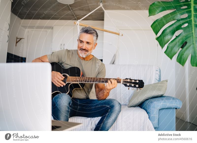 Elderly guitarist performing music on sofa near laptop man musician loft instrument interior acoustic play online headphones chill couch meloman aged hobby