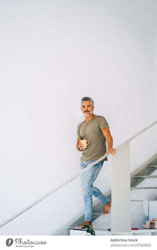 Aged male on steps with tea cup man staircase stairway loft interior drink beverage banister hot drink aged senior coffee fence handrail mug railing elderly old