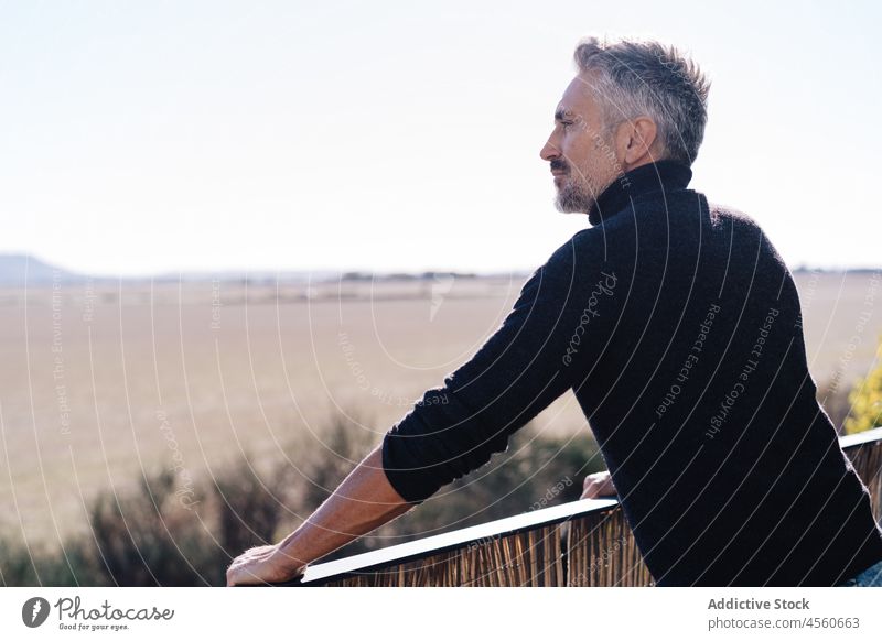 Elderly man standing on balcony landscape admire contemplate observe railing view sky male old terrace serene fence aged senior elderly gray hair peaceful dream