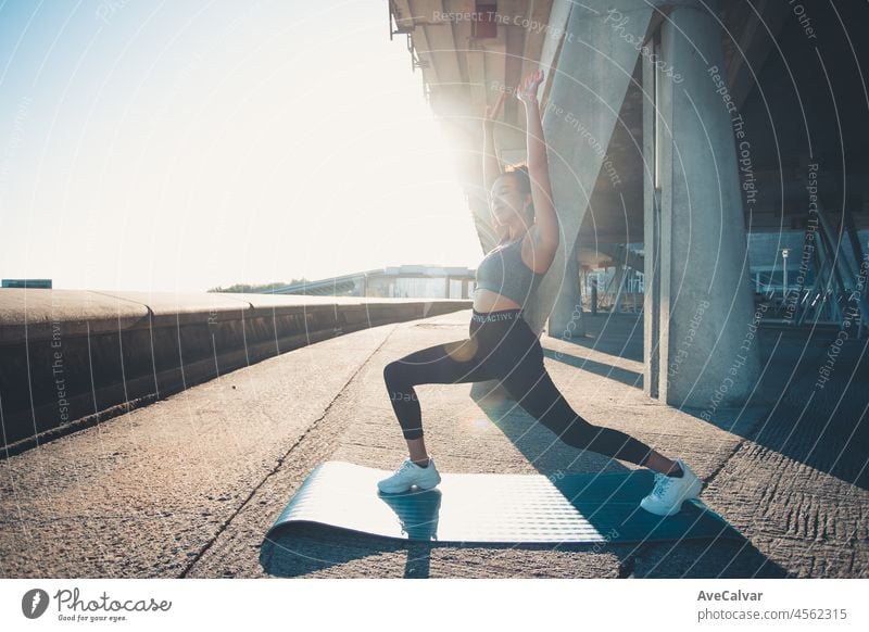 Beautiful girl athlete, african tanned skin. Smiles to camera while Warms up muscles before doing urban yoga training.Leg joints articular gymnastics. Music while training.Leggings clothing and top.