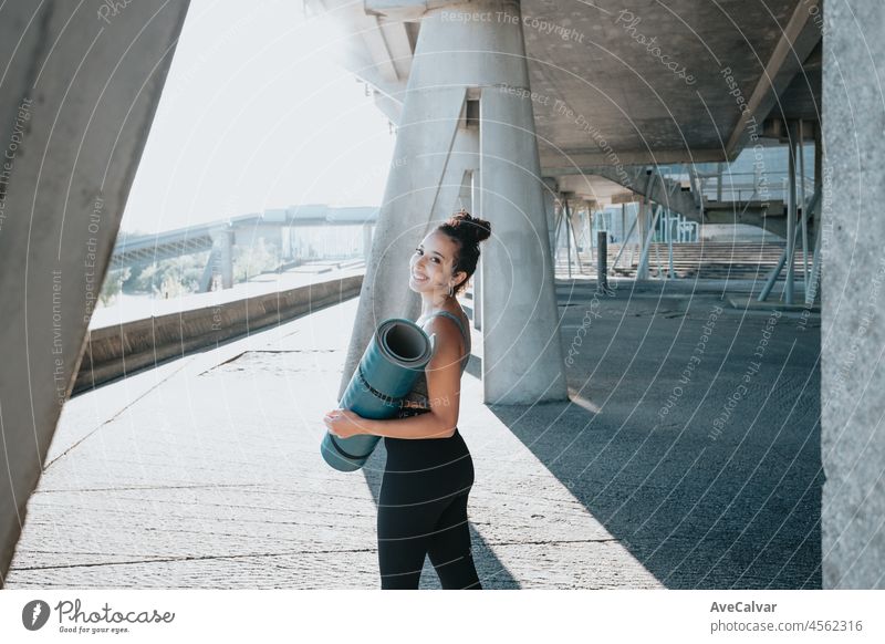 Portrait of a smiling young african arab woman smiling after jogging at outdoors. Holding a yoga mat, urban relax sport. Urban exercise outdoors. young adult