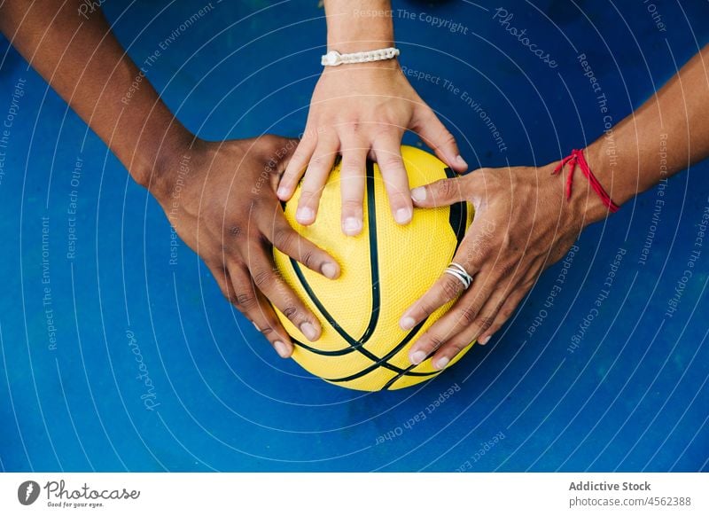 Crop faceless diverse players putting hands on ball man basketball game streetball activity together team sport competition prepare court yellow men young