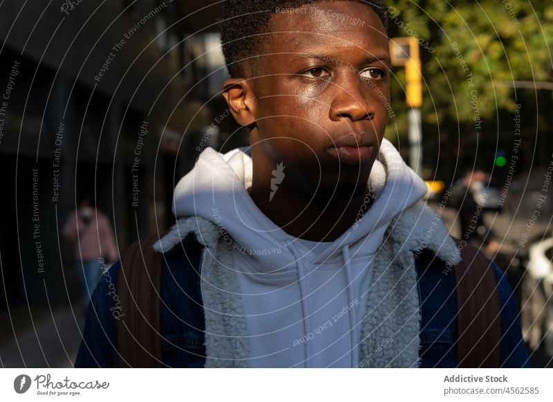 Serious black man standing on street in sunlight trendy ethnic appearance individuality confident serious pensive male african american calm thoughtful