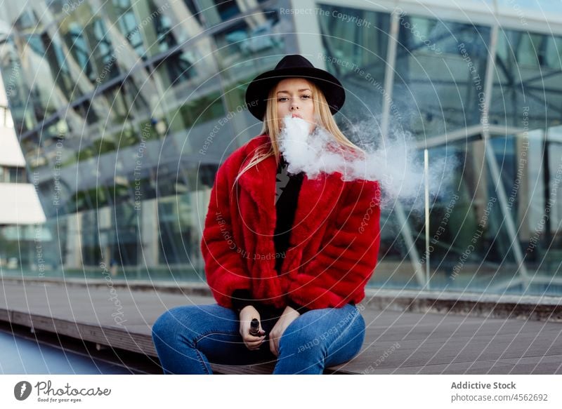 Blonde young woman smoking with vaper machine on the street vaping vaporizer adult alternative attractive beautiful hat blonde blow caucasian smoke cigarette