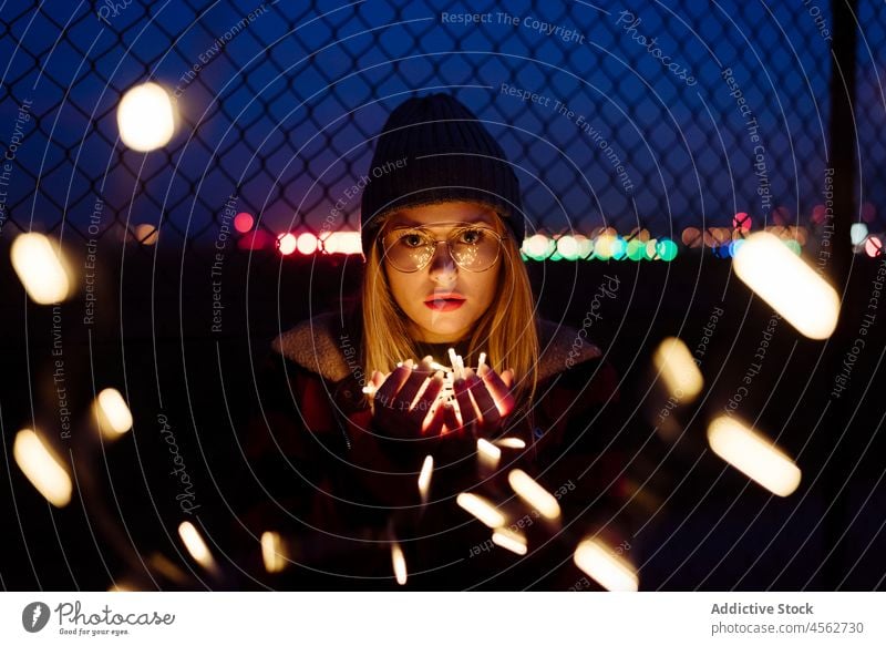 Young woman with wool hat and glasses holding a light garland young night portrait attractive autumn blonde bokeh bulbs candid caucasian city creativity cute