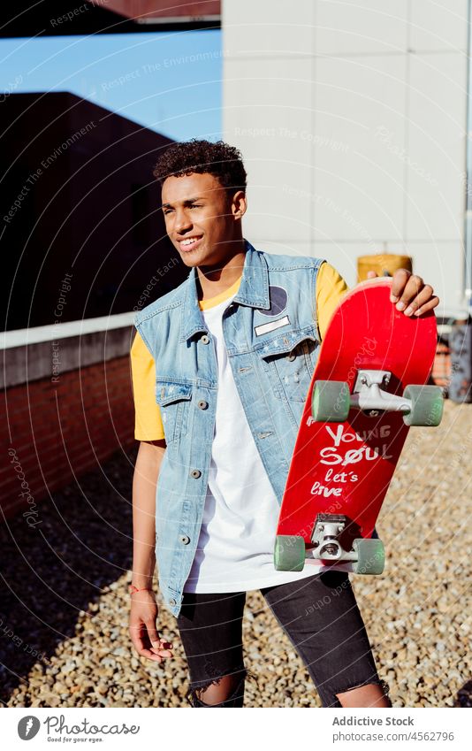 Handsome young black man with a skateboard on the street male boy happy smile portrait backstreet urban city brick wall rooftop vest patches handsome attractive