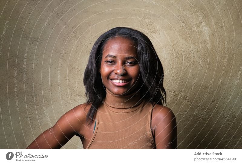 Smiling black female in dress standing against beige wall woman pensive thoughtful appearance individuality personality feminine outfit model charm