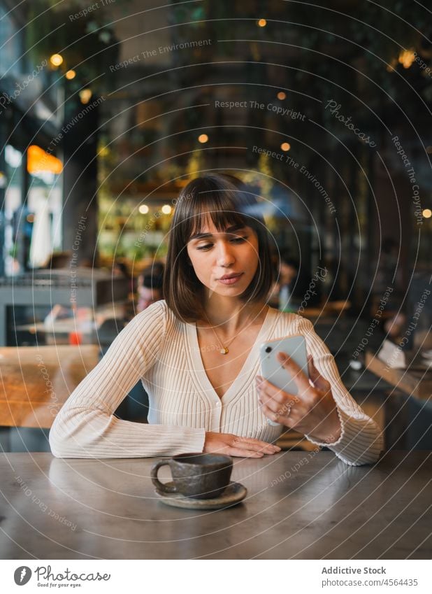 Young woman checking messages on smartphone in cafe coffee chat cup using drink mobile gadget device online connection communicate browsing relax casual surfing